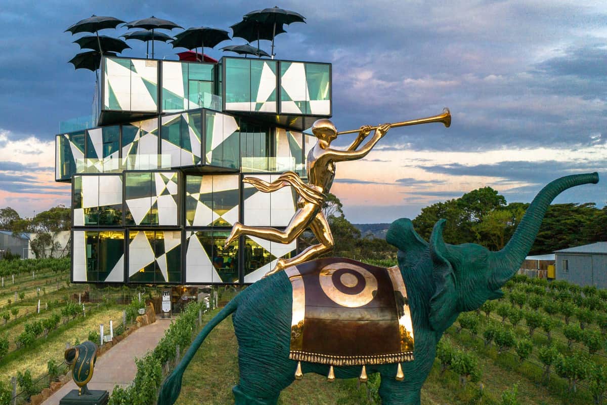 Modern building with geometric design behind a gold statue of a person blowing a trumpet, riding a decorated elephant.