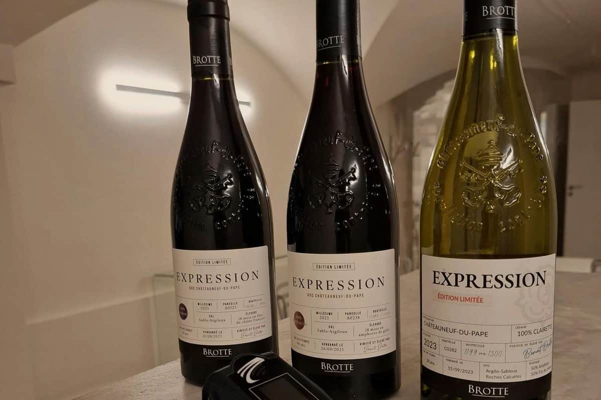 Three bottles of Brotte wine labeled "Expression," with one yellow and two dark, placed on a table next to a digital device.