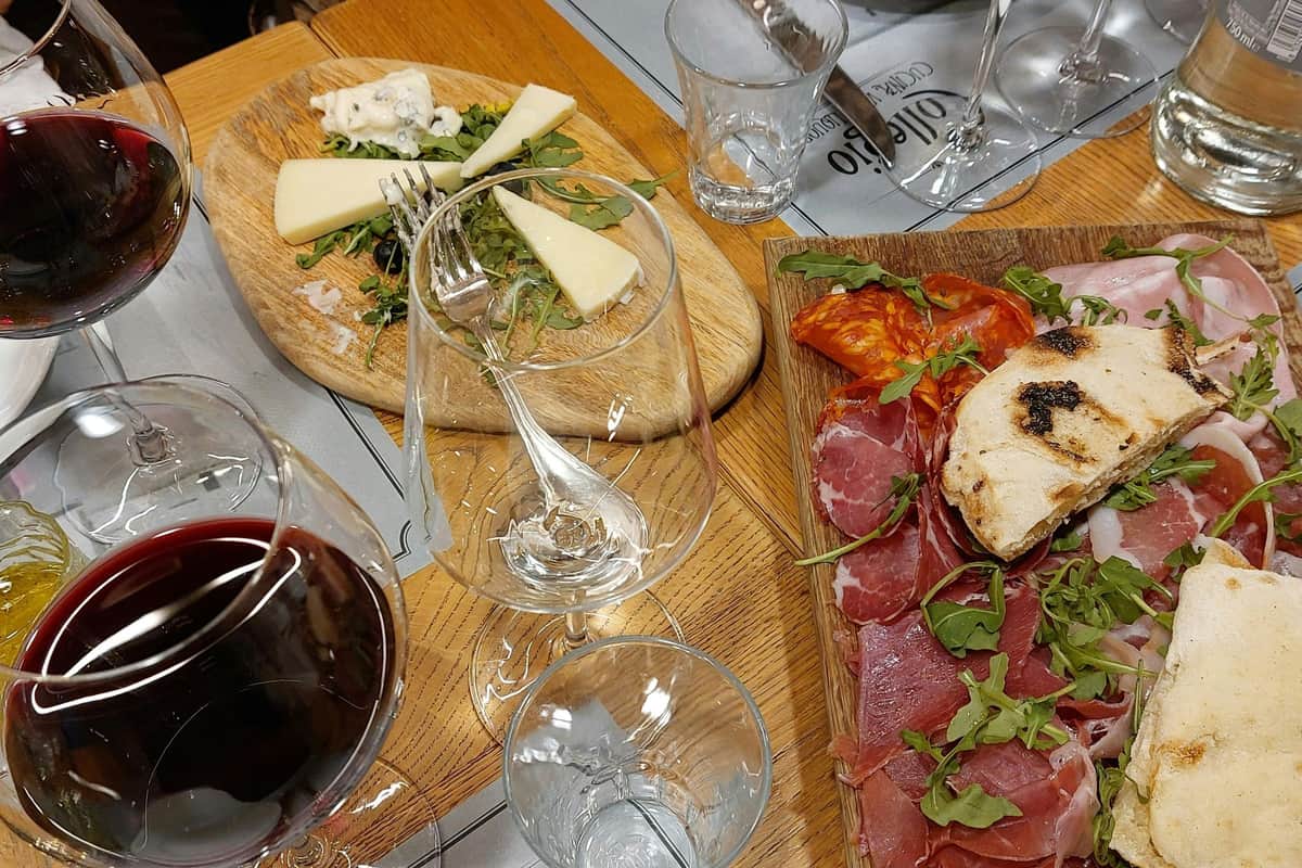 Rome: Guided Wine & Olive Oil Tasting + Lunch A charcuterie board with meats, cheese, arugula, and a glass of red wine on a wooden table.