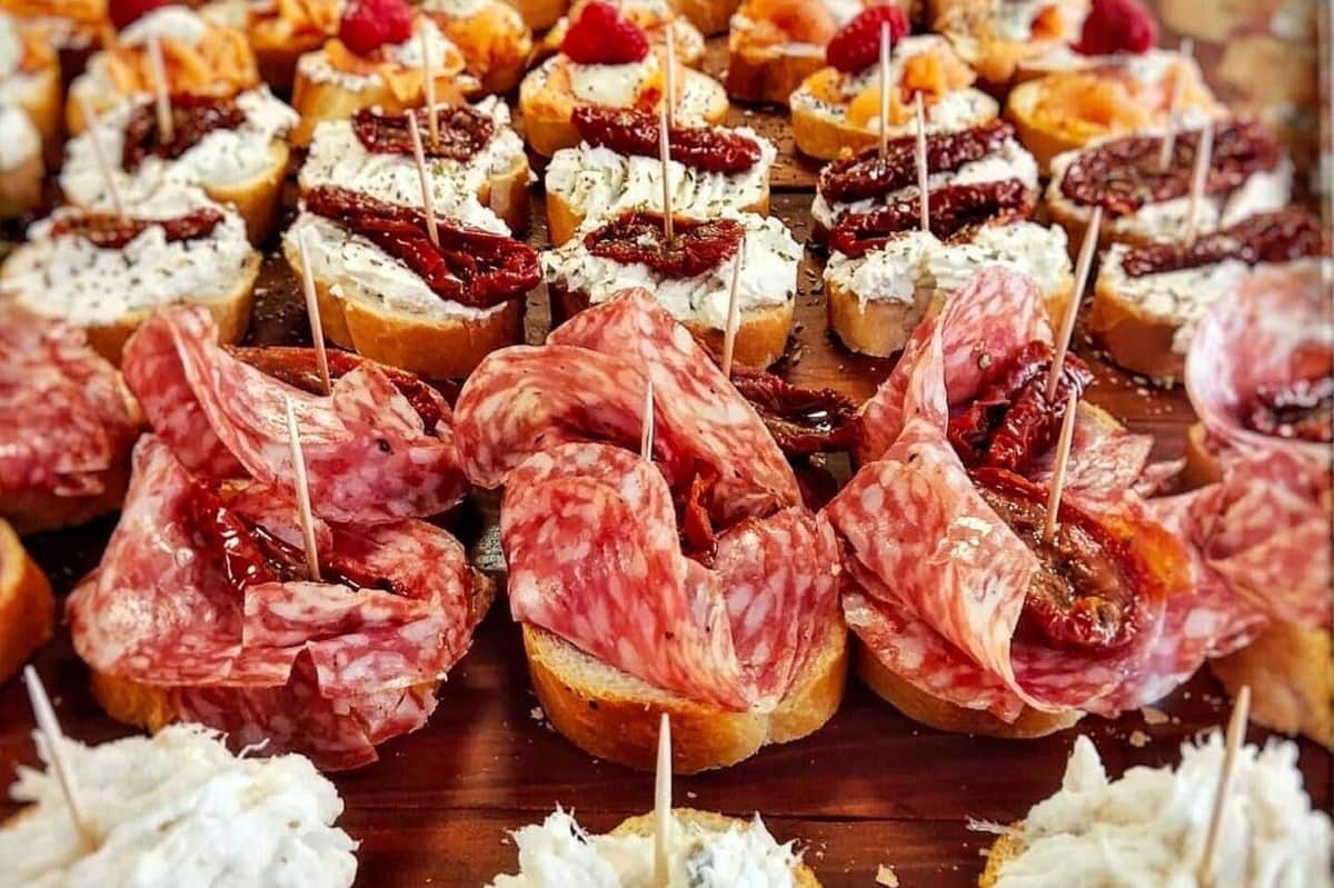 A close-up of various appetizers on small bread slices, topped with meats, cheeses, dried tomatoes, and garnishes.