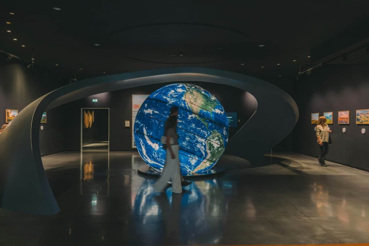 WOW Porto Museums & Taylor's Port: Entry Ticket + Chocolate & Wine Tastings A person walks past a large illuminated globe display in a dark exhibition space with modern design elements.