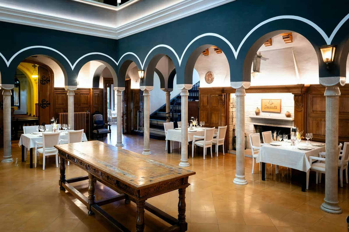 Codorníu Winery: Guided Tour + La Torre Menu Lunch + Cava Tasting Elegant dining area with arched columns, wooden furniture, and decorative elements, featuring a central wooden table.