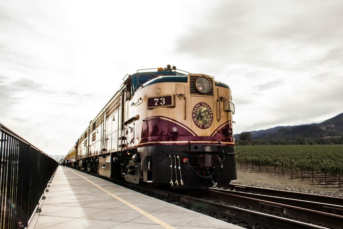 A vintage train with the number 73, labeled "Napa Valley Wine Train," on tracks next to a vineyard under a cloudy sky.