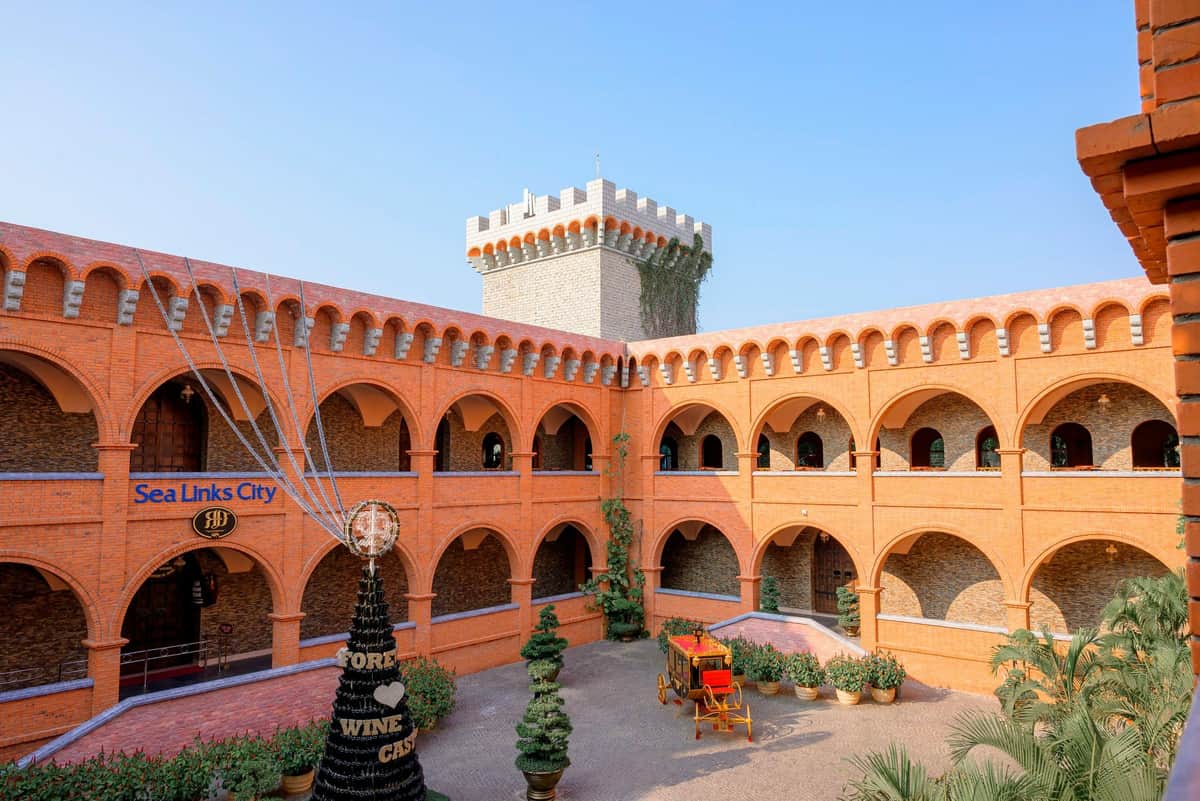 RD Wine Castle Mui Ne: Admission + 3 Glasses of Wine A courtyard with orange arched walls, a central Christmas tree structure, potted plants, and a visible tower in the background.