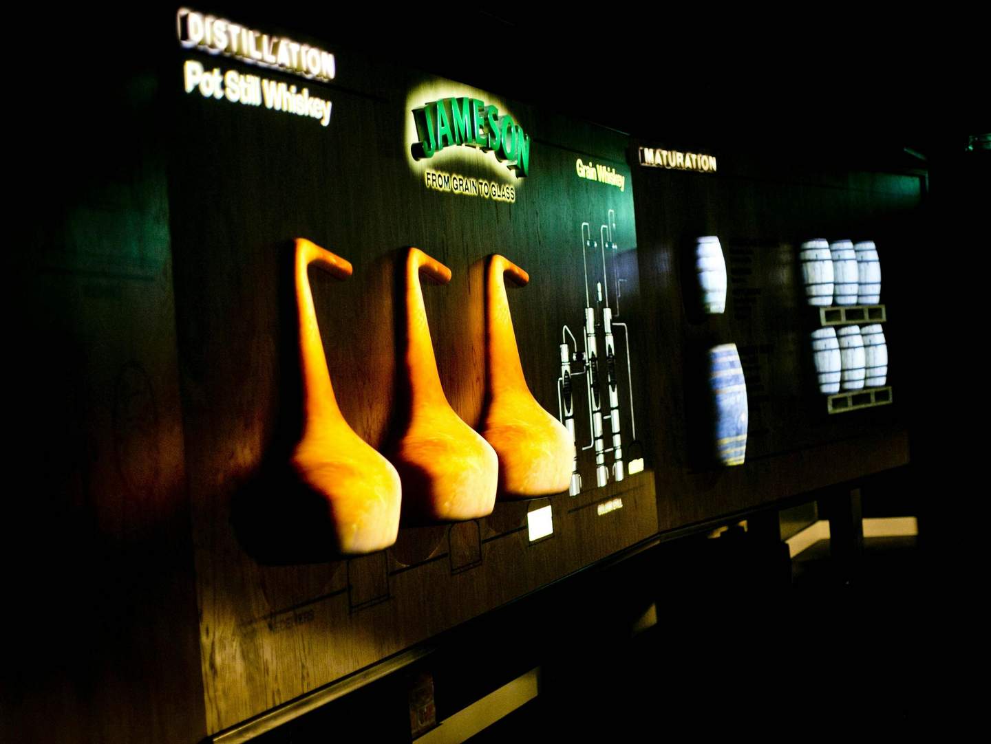 Jameson Distillery Bow St. Backlit display showing different stages of whiskey production: distillation, grain whiskey, and maturation with accompanying images.